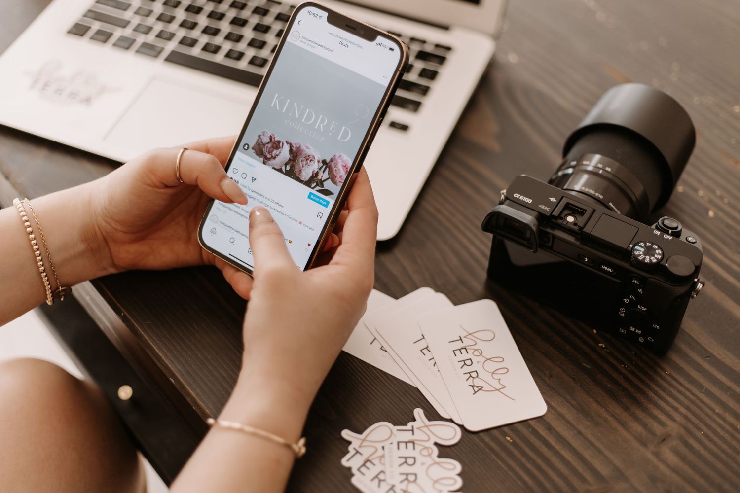 Hands holding smartphone and laptop with business cards on wooden desk.