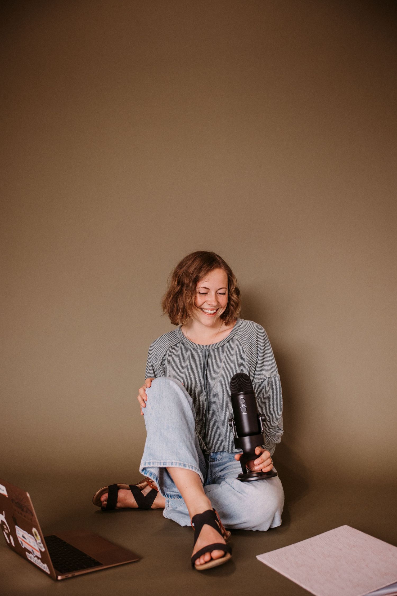 Person wearing gray shirt sits casually on floor with sandals and laptop.