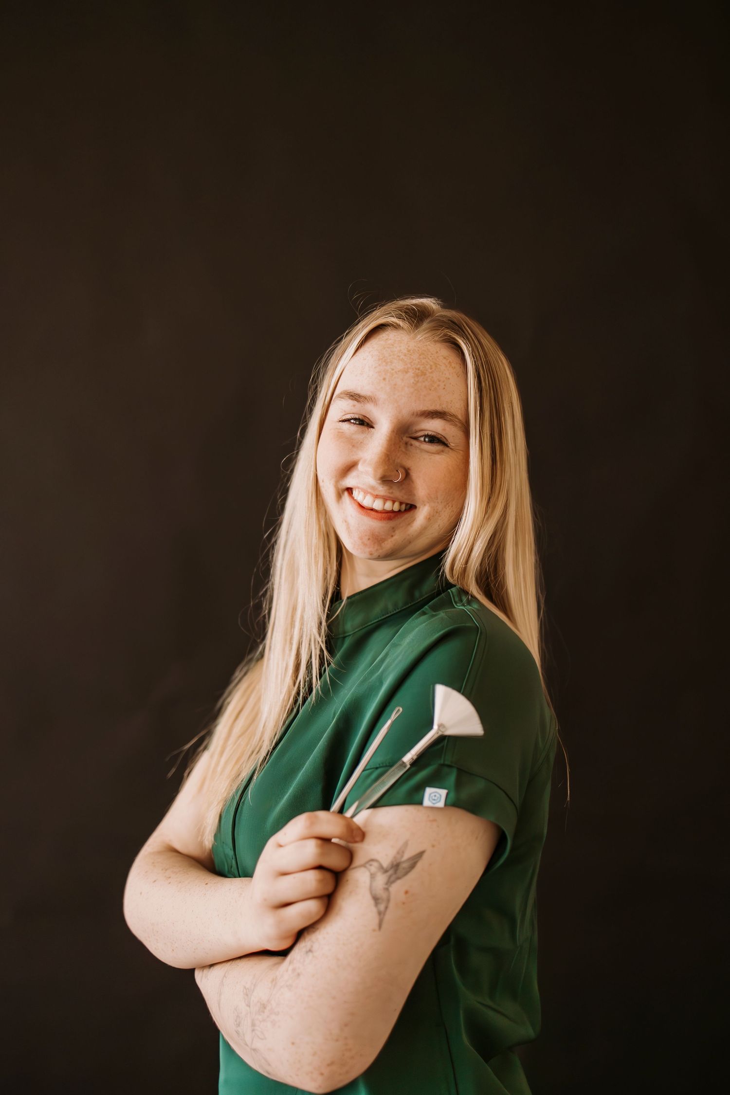 Portrait against dark background showing person in green shirt displaying arm.