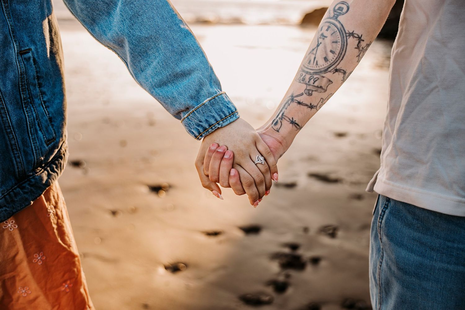 Close-up shots of tattooed hands holding each other against a beach sunset backdrop.
