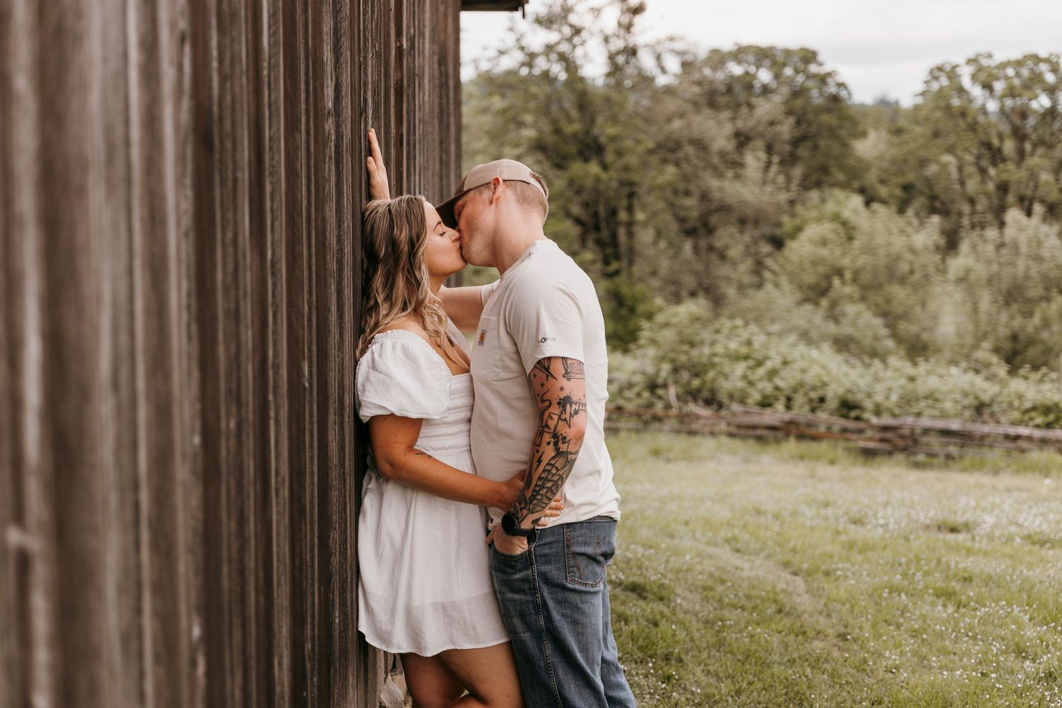 Loving couple poses together near rustic barn wall in natural outdoor setting.
