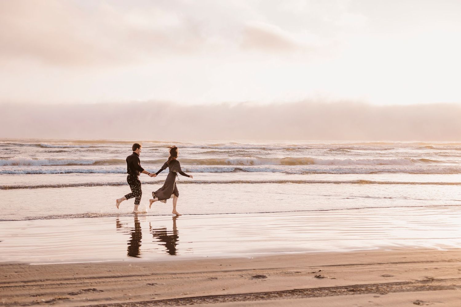 Two silhouettes dance together on a beach at sunset with waves rolling in.