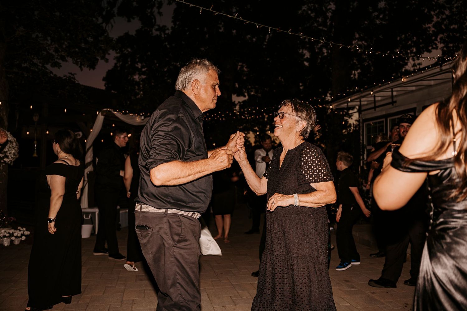Guests dance together during an evening wedding reception under string lights.