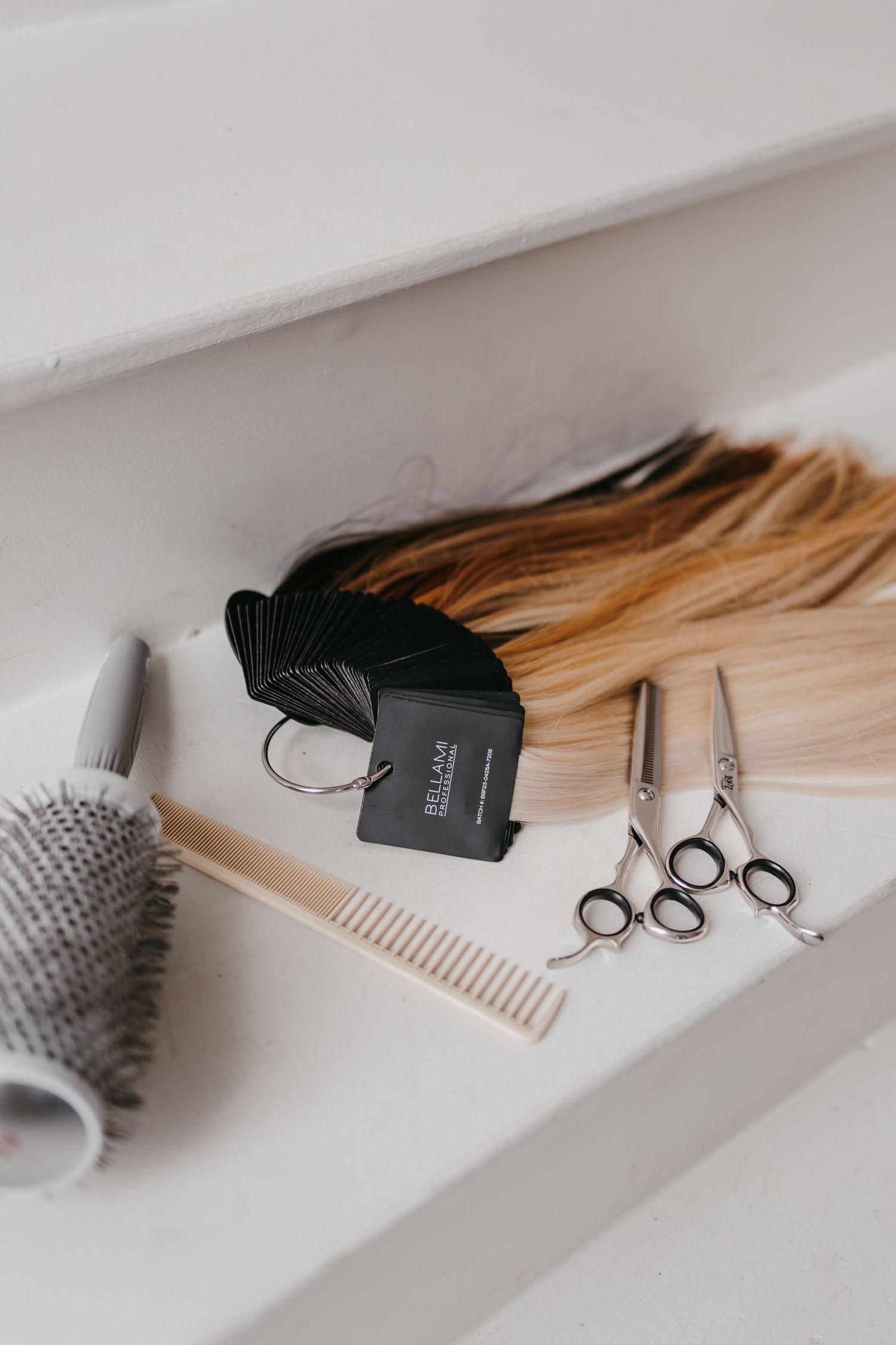 Flat lay of hair styling tools including brushes, combs and scissors on white surface.