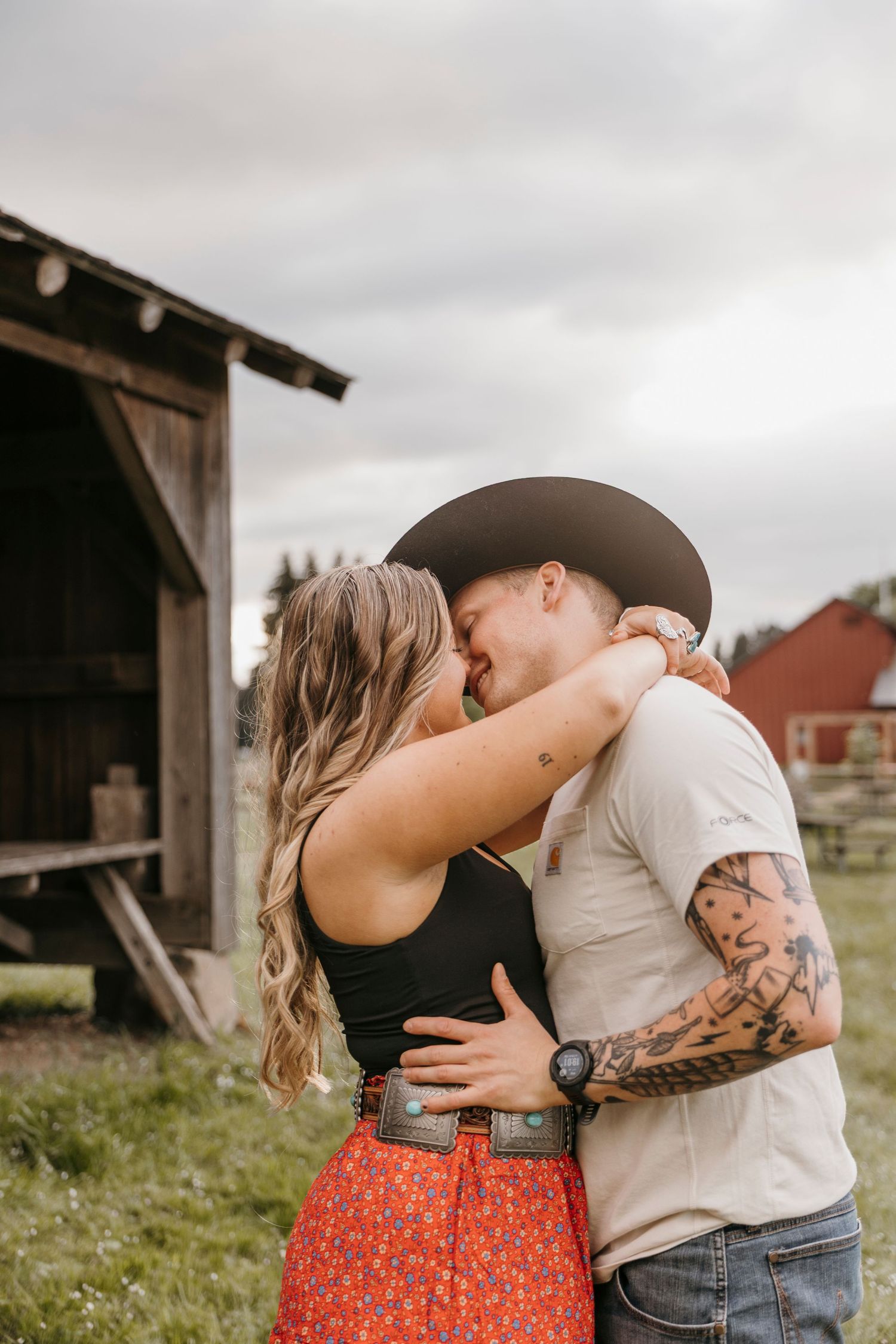 Intimate couple portraits against rustic barn backdrop with red floral skirt and tattoo details.