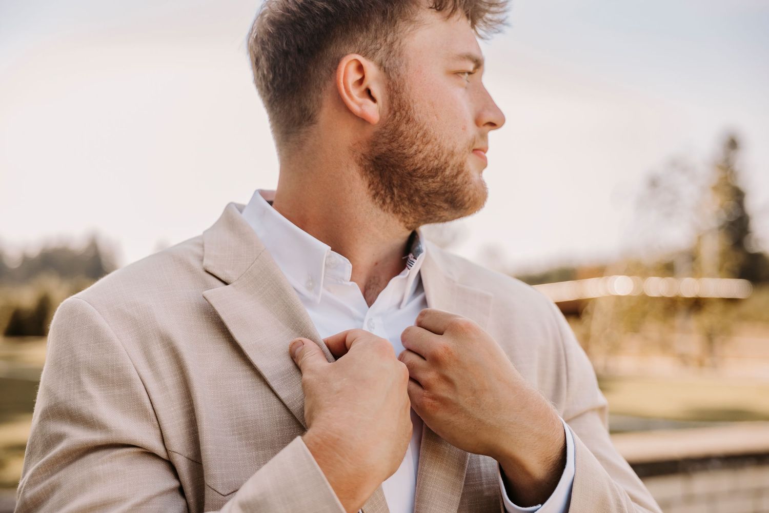 Close-up profile of groom adjusting his tie in warm natural light.