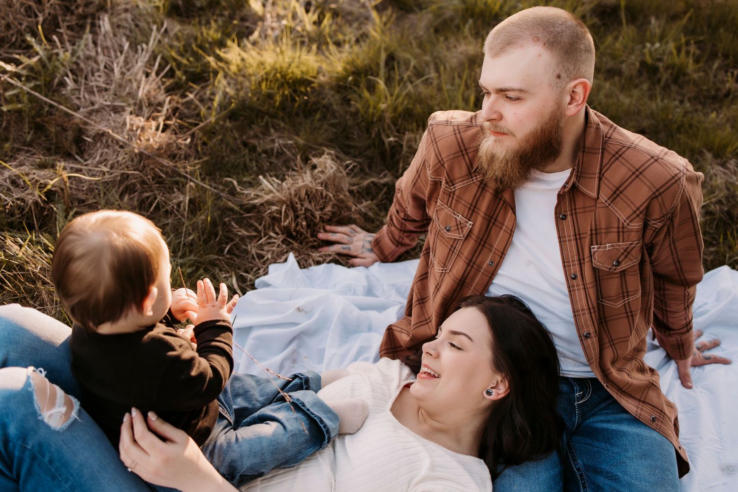 Family relaxing together on picnic blanket during outdoor photoshoot.