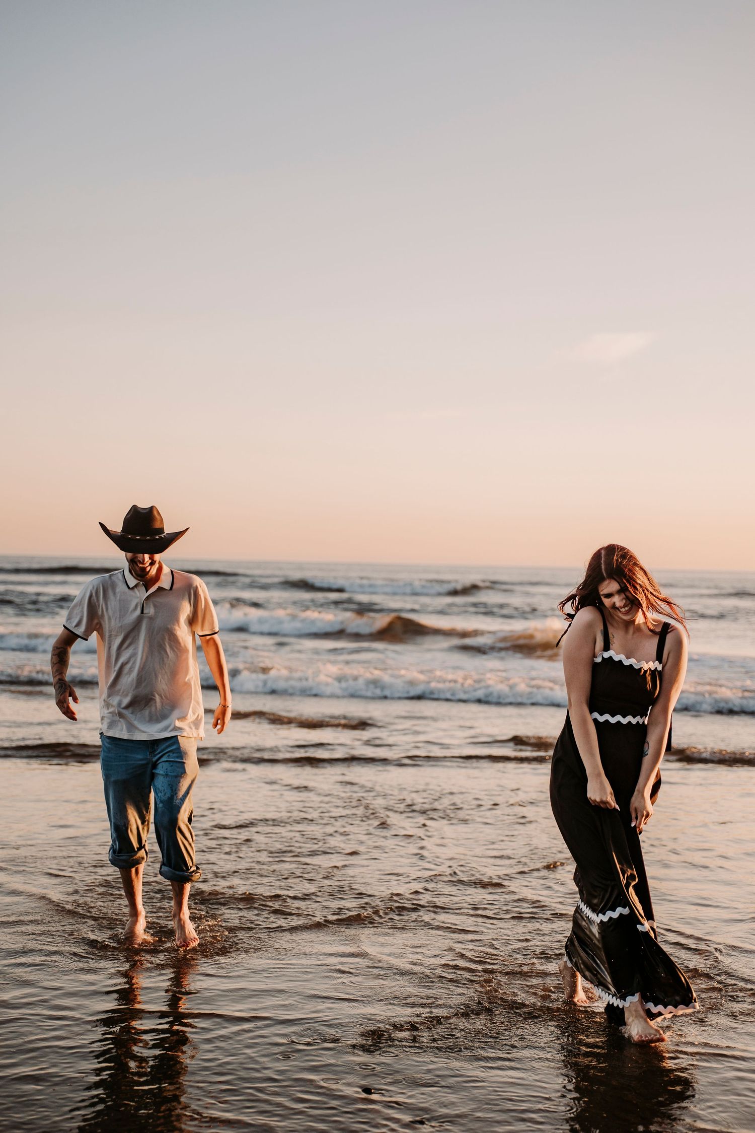 Couple splashing and playing in ocean waves during golden hour at the beach.
