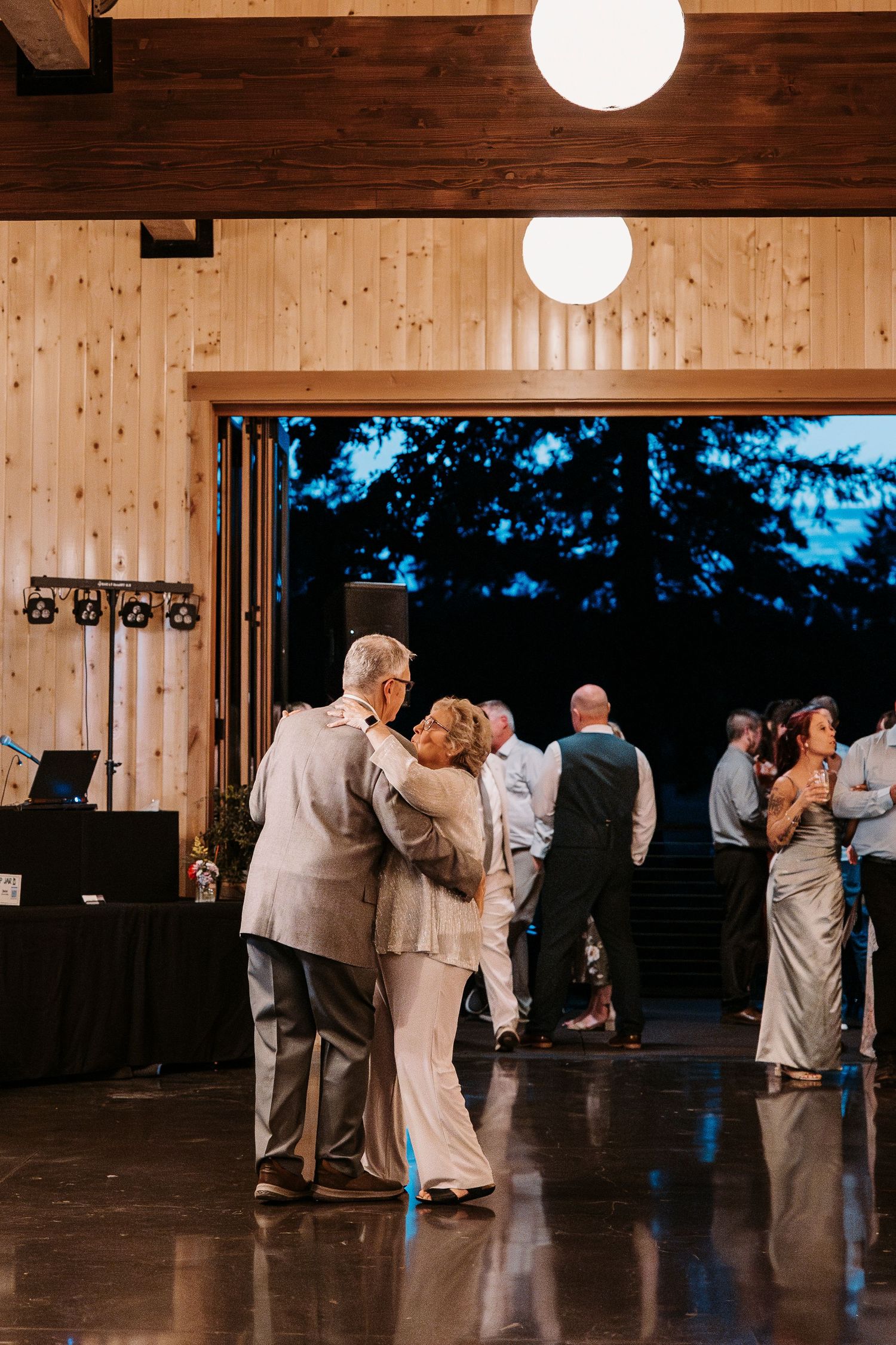 Couples dancing together on a wooden floor under round pendant lights in a rustic venue.