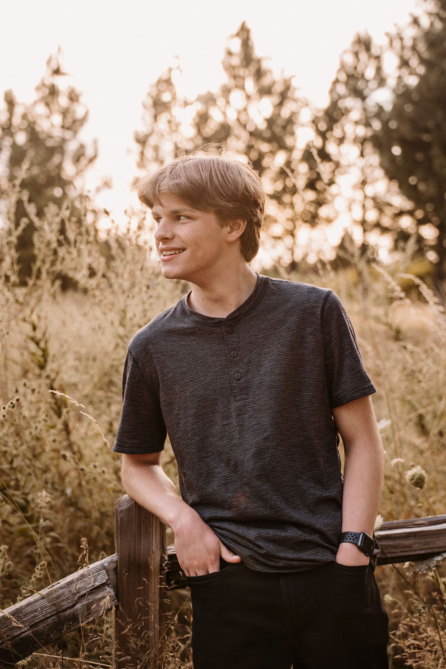 Portrait of person in black t-shirt leaning on wooden fence at sunset with golden light.