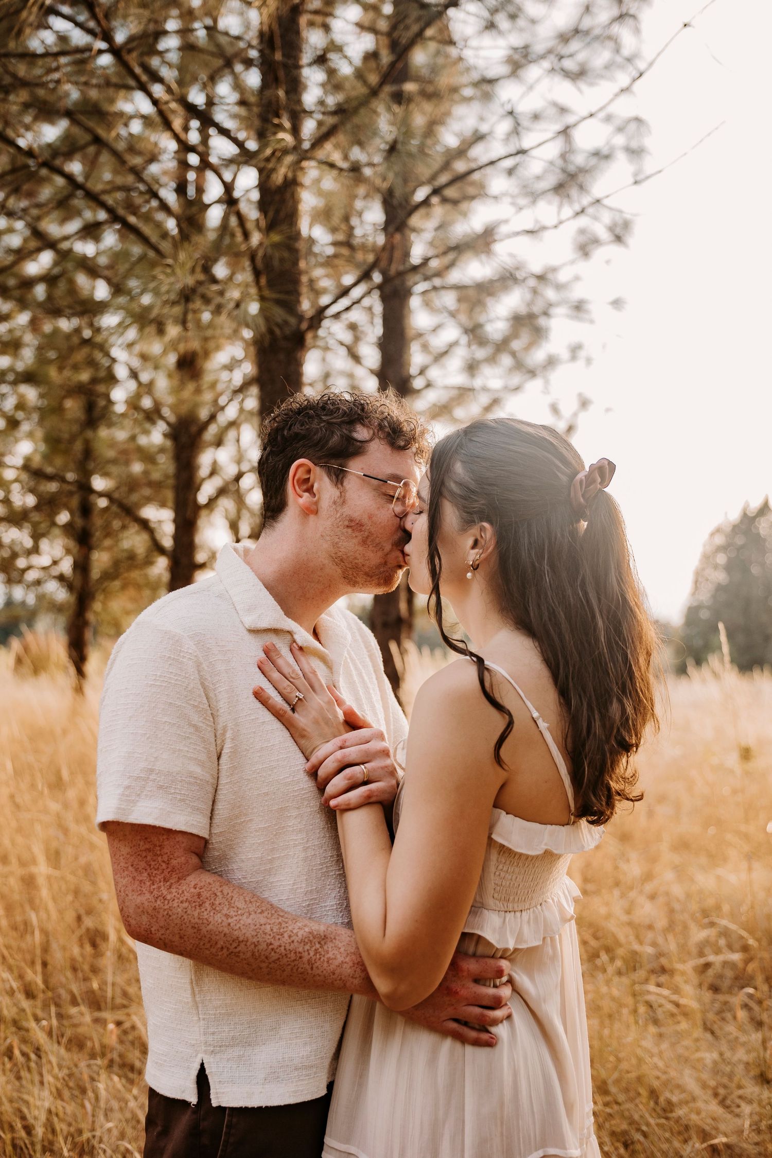 Intimate couple portraits in a sun-drenched field surrounded by tall pine trees.