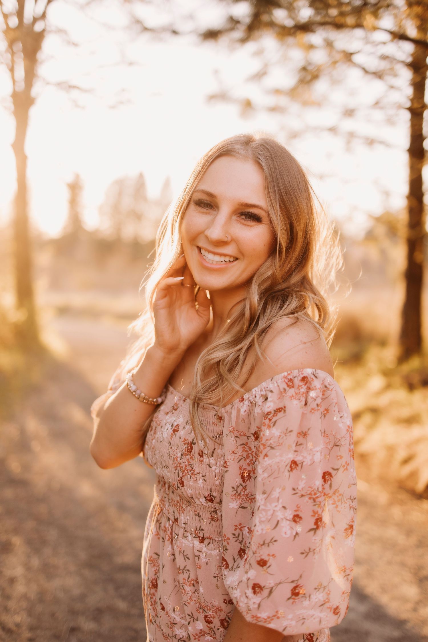 Sunset portrait in floral dress with golden backlight filtering through trees.