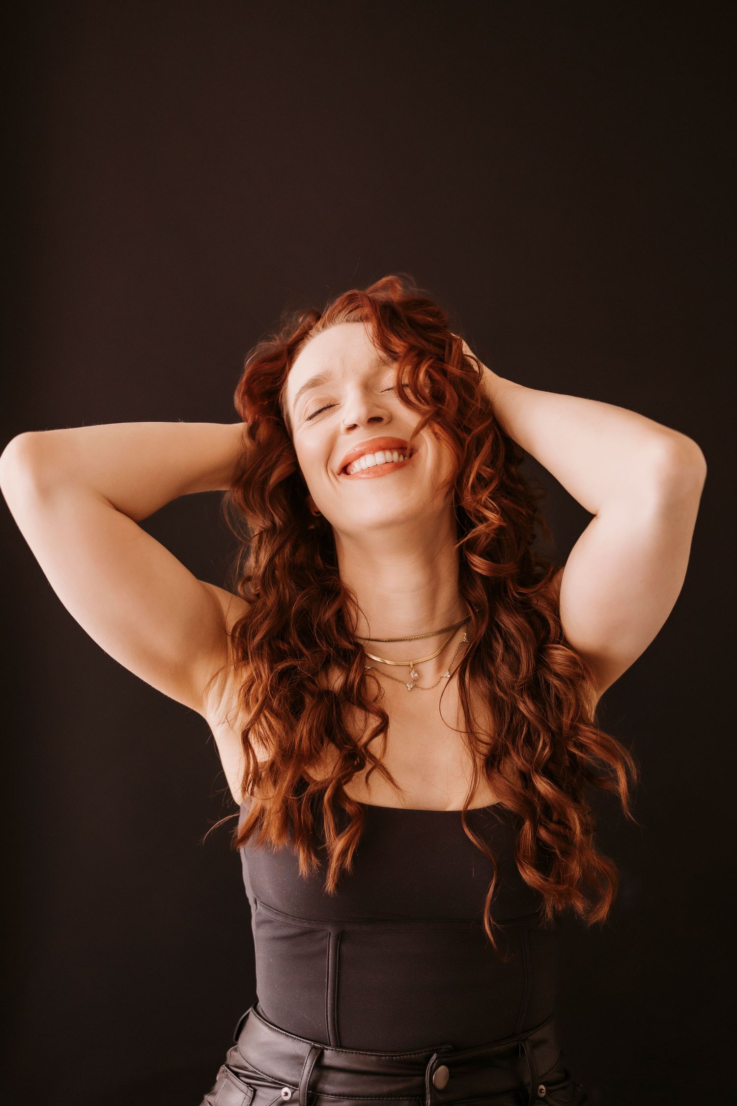 Joyful studio portrait showing natural curls and genuine expression against dark backdrop.