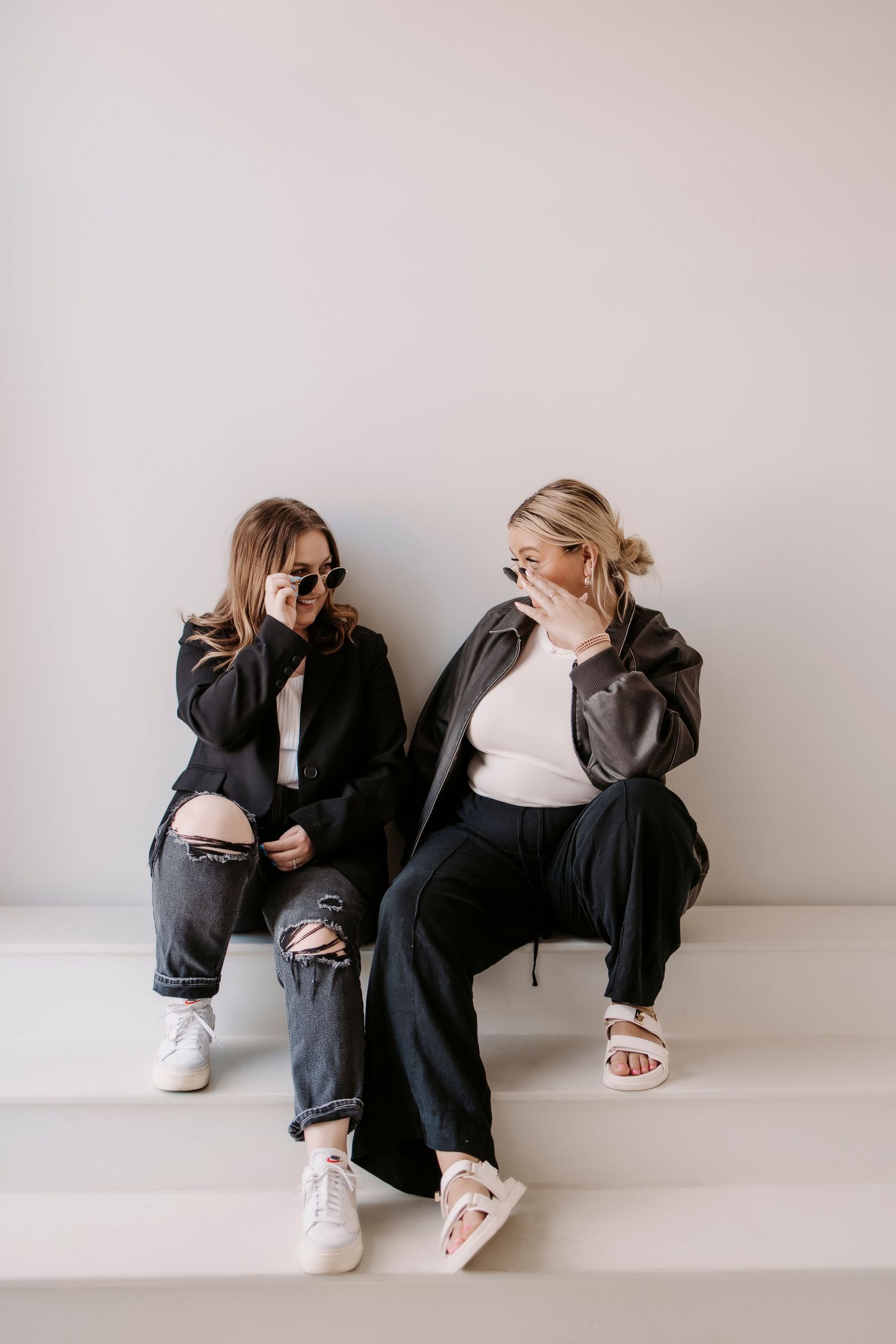 Two people in casual attire sitting together against a white wall in a minimalist setting.