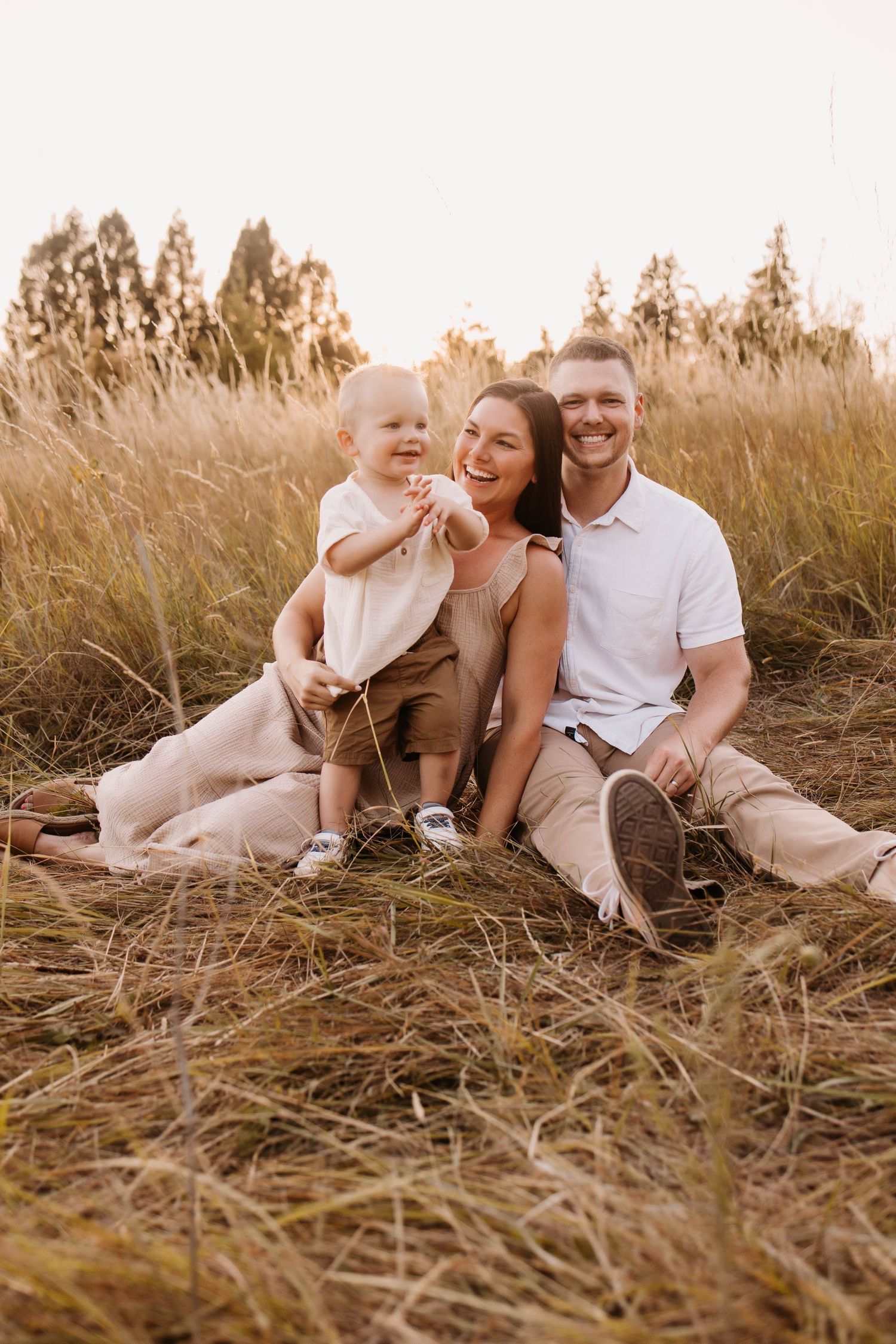 Family relaxing together in a golden field during sunset wearing neutral tones.