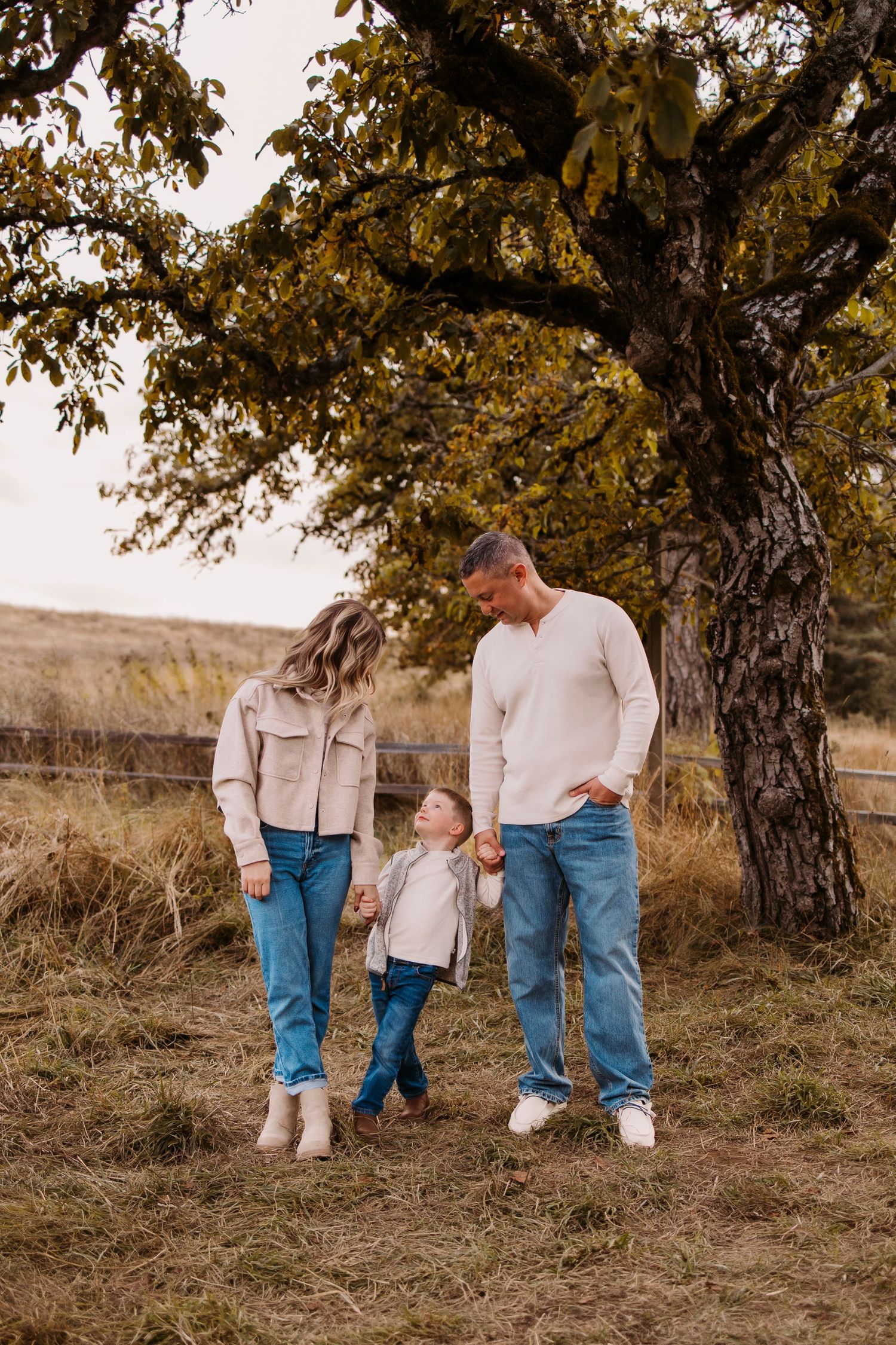 Family photo session under an autumn tree showing only legs and feet in casual attire.