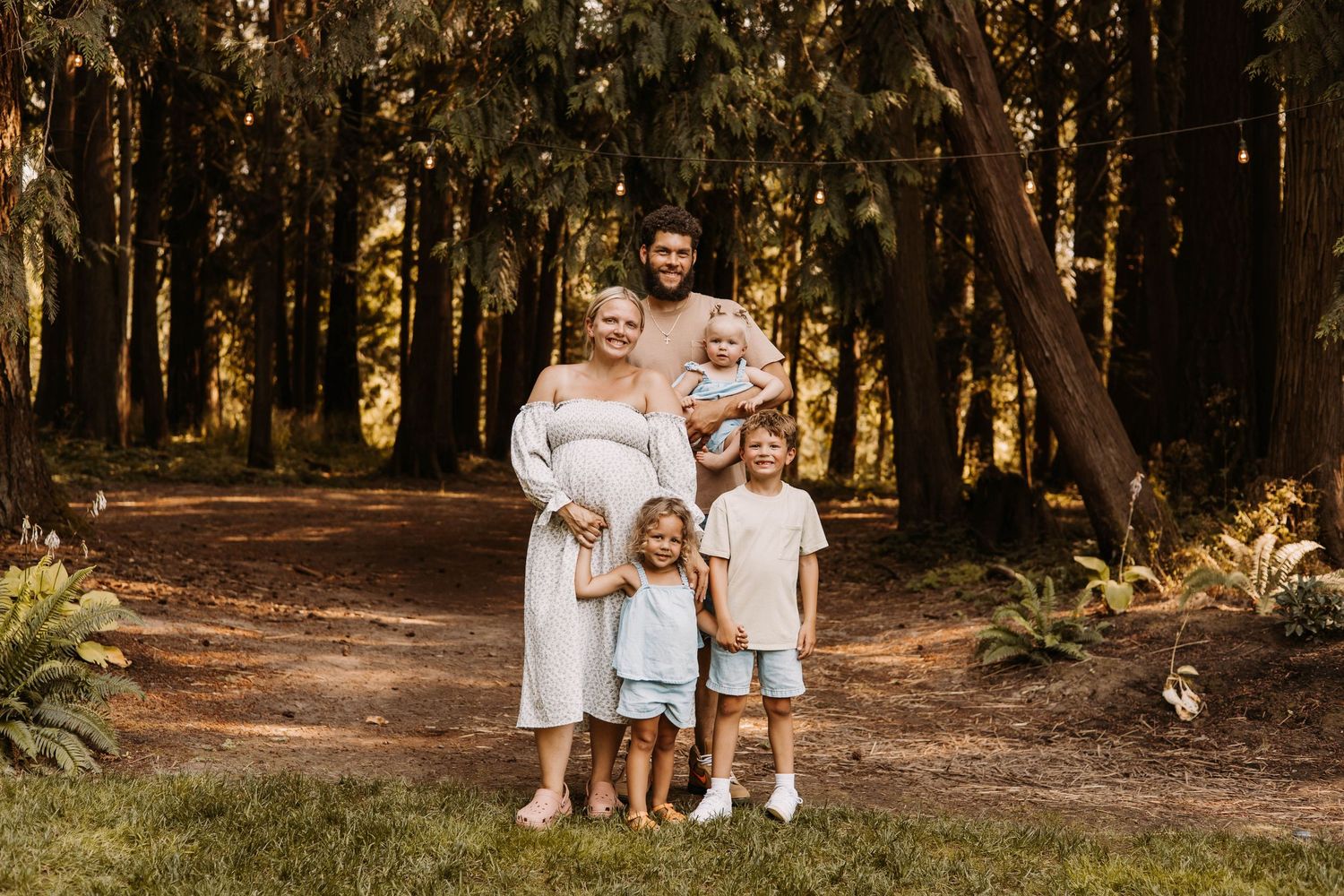 Family walking together through a sunlit forest path wearing coordinated white outfits.