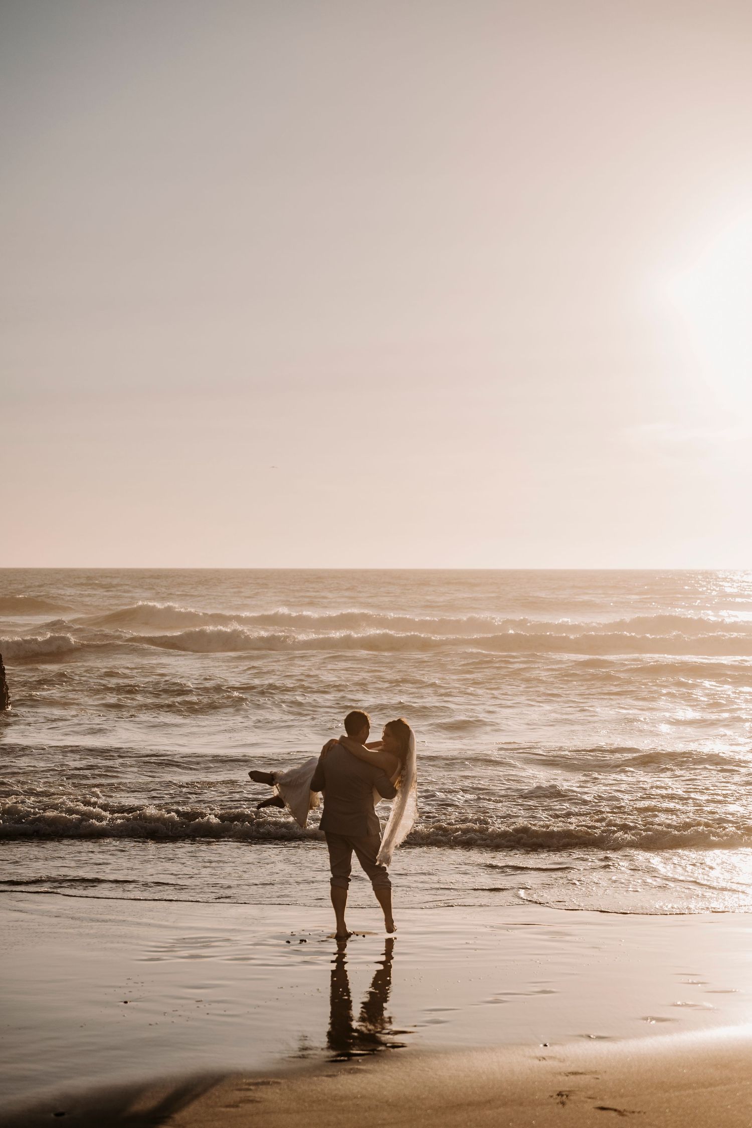 Silhouettes of couple walking along beach shoreline at golden hour.