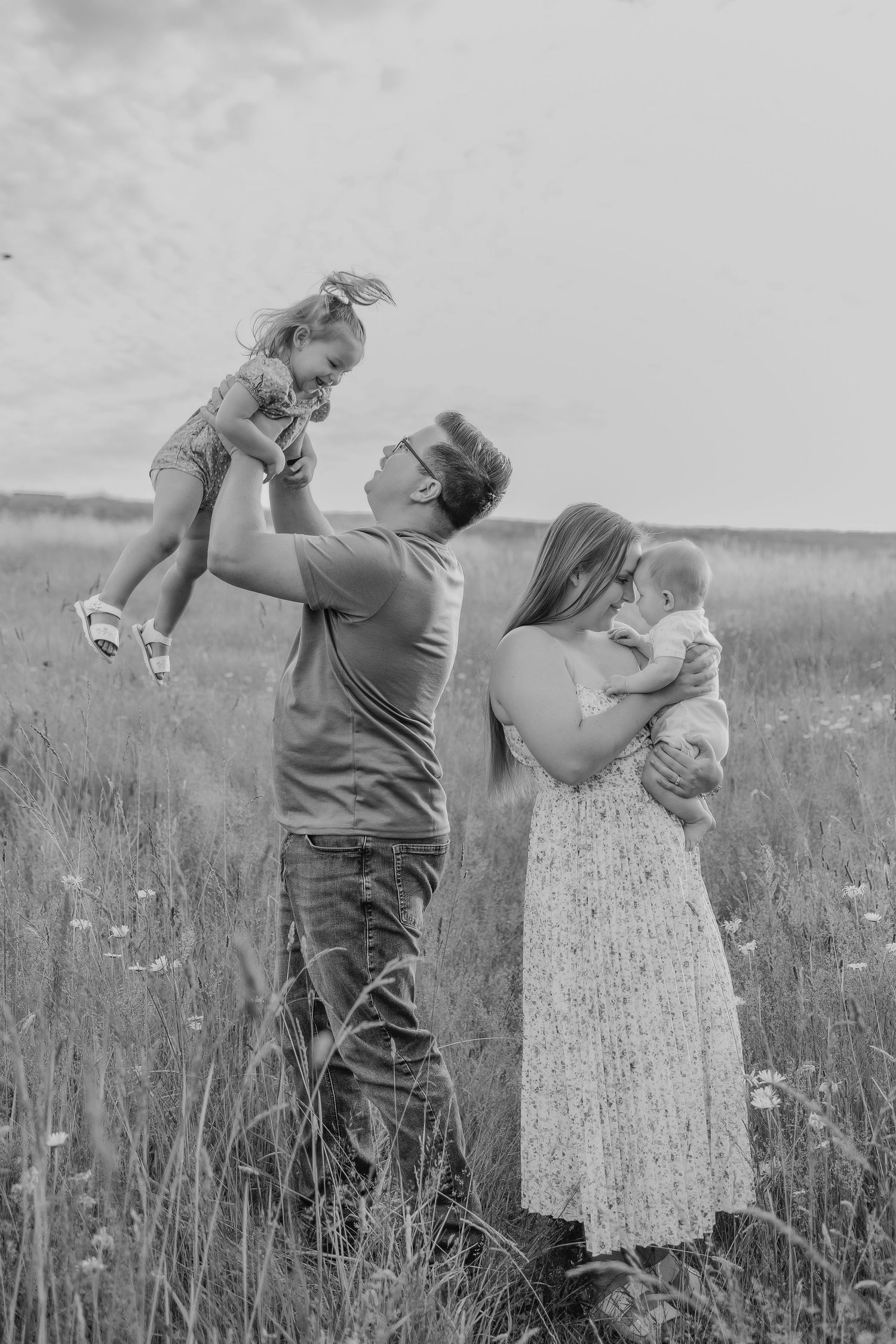 Black and white portrait of family sharing tender moments in meadow.