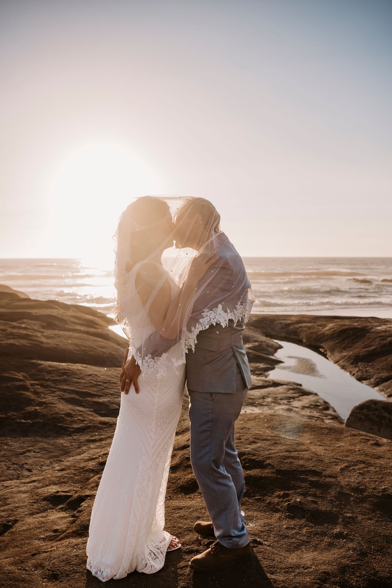 Romantic sunset photoshoot on rocky coastal cliffs with ocean waves in the background.