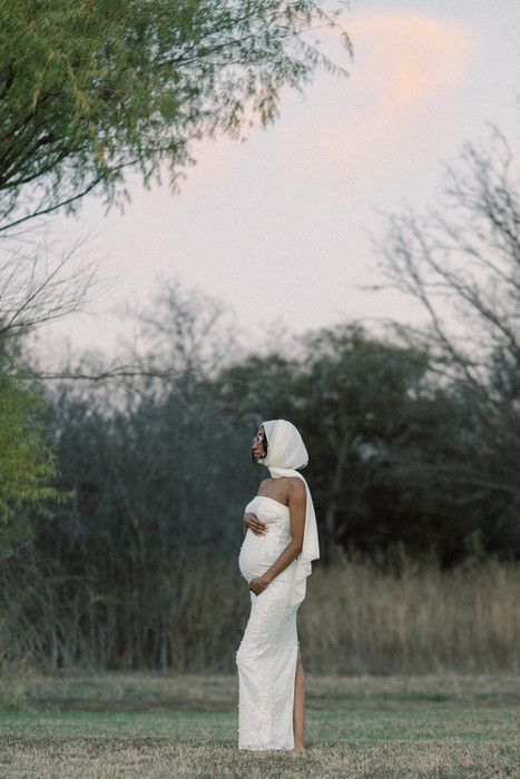 A figure in white poses gracefully against a sunset sky and tree-lined background.