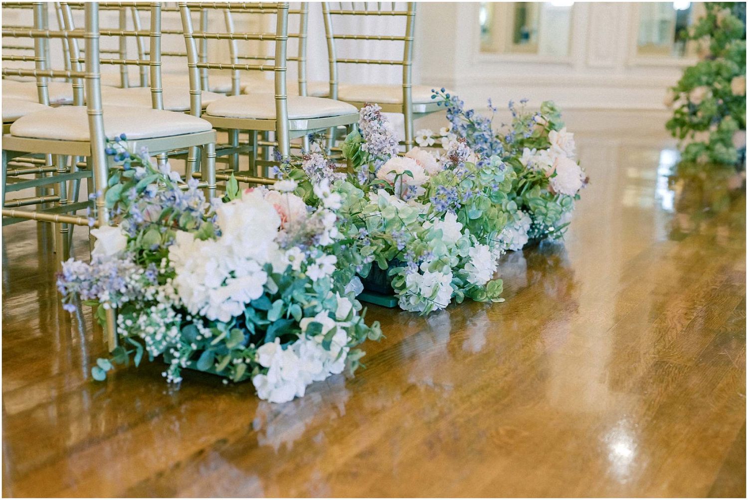 Beautiful blue and white floral arrangements line a polished wooden floor at an elegant wedding venue.