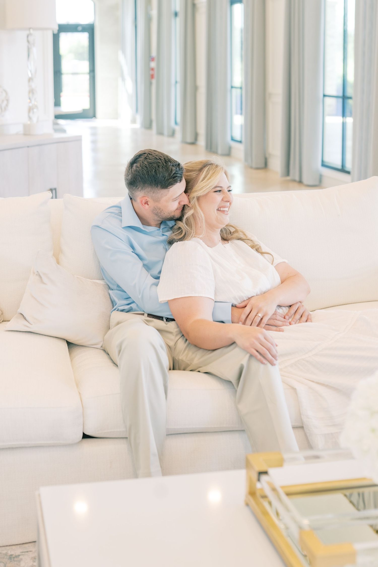 Couple sitting together on a cream sofa, smiling and laughing in a bright elegant living room.