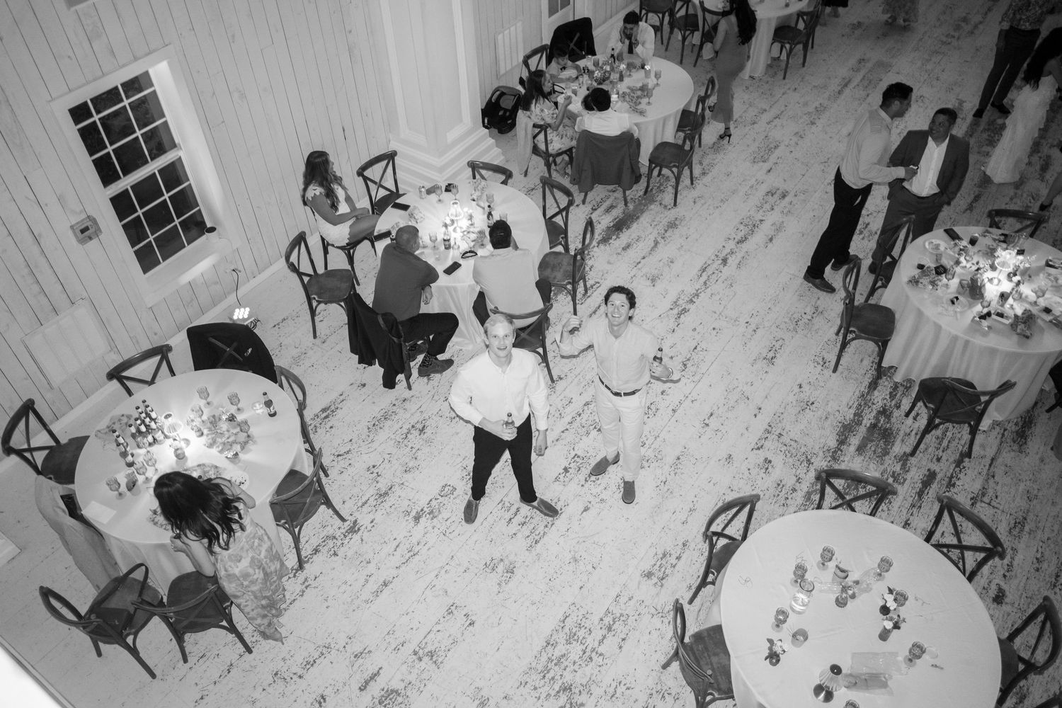 Aerial black and white view of wedding reception guests mingling on whitewashed barn floor.