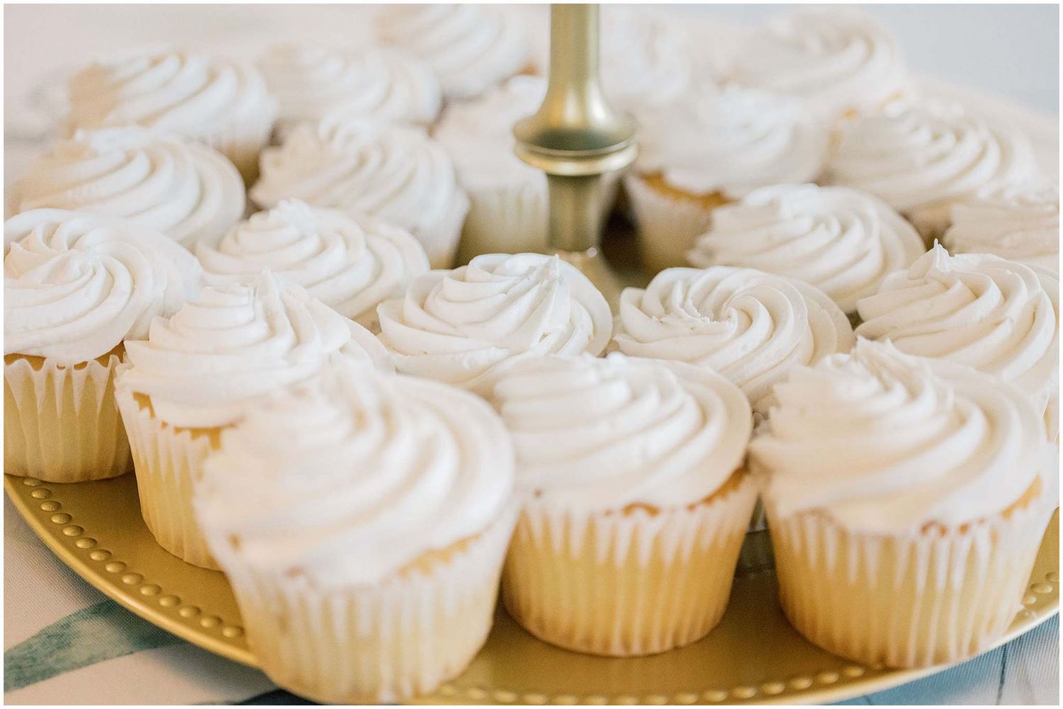 Homemade vanilla cupcakes with swirled white frosting arranged in rows on a serving platter.