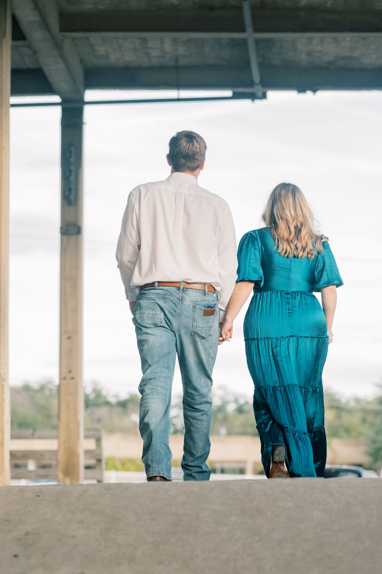 A couple in coordinated casual outfits walking together on a covered patio with a scenic background.