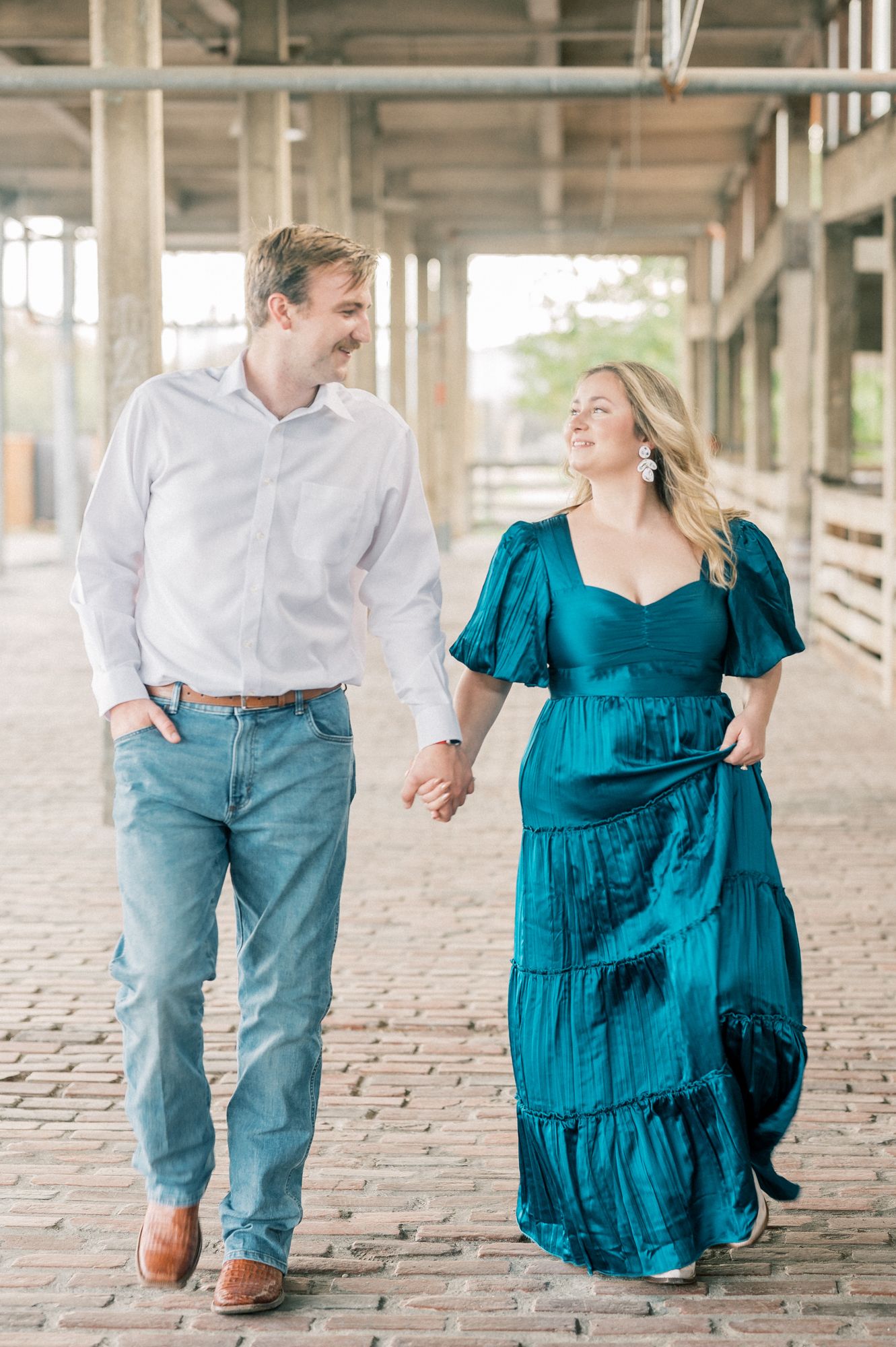A couple walks together on a brick pathway, with the woman wearing a teal dress and the man in light colored clothing.