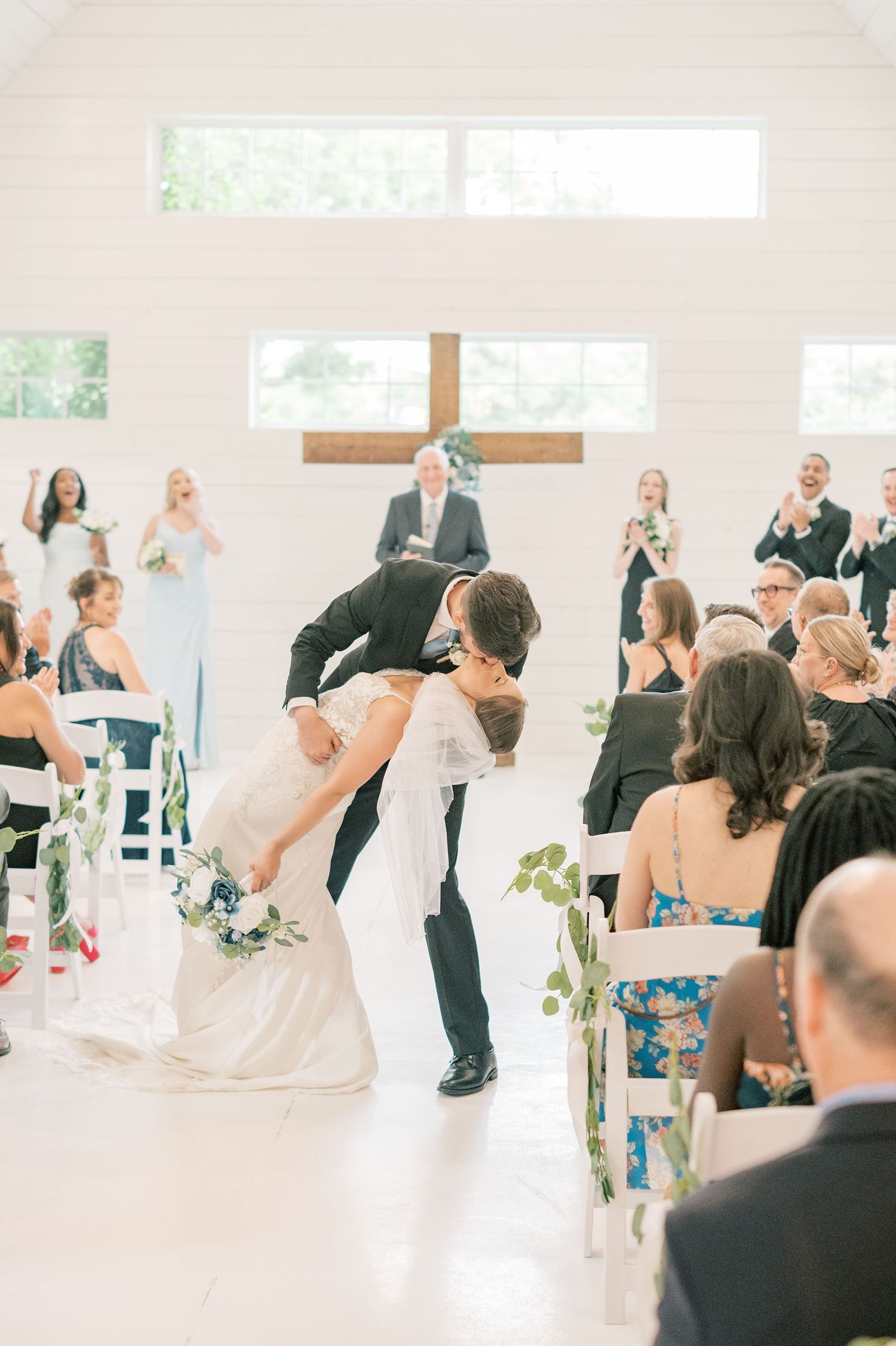 Wedding ceremony candid moments captured in a bright white church with guests looking on.