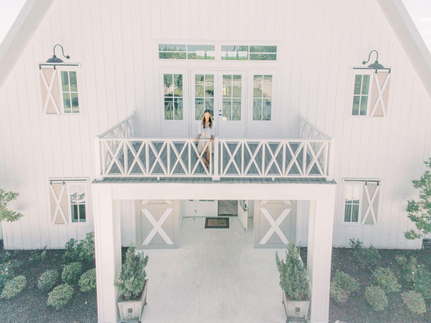 Elegant white farmhouse barn venue with balcony railing, barn doors, and gooseneck lights for weddings.