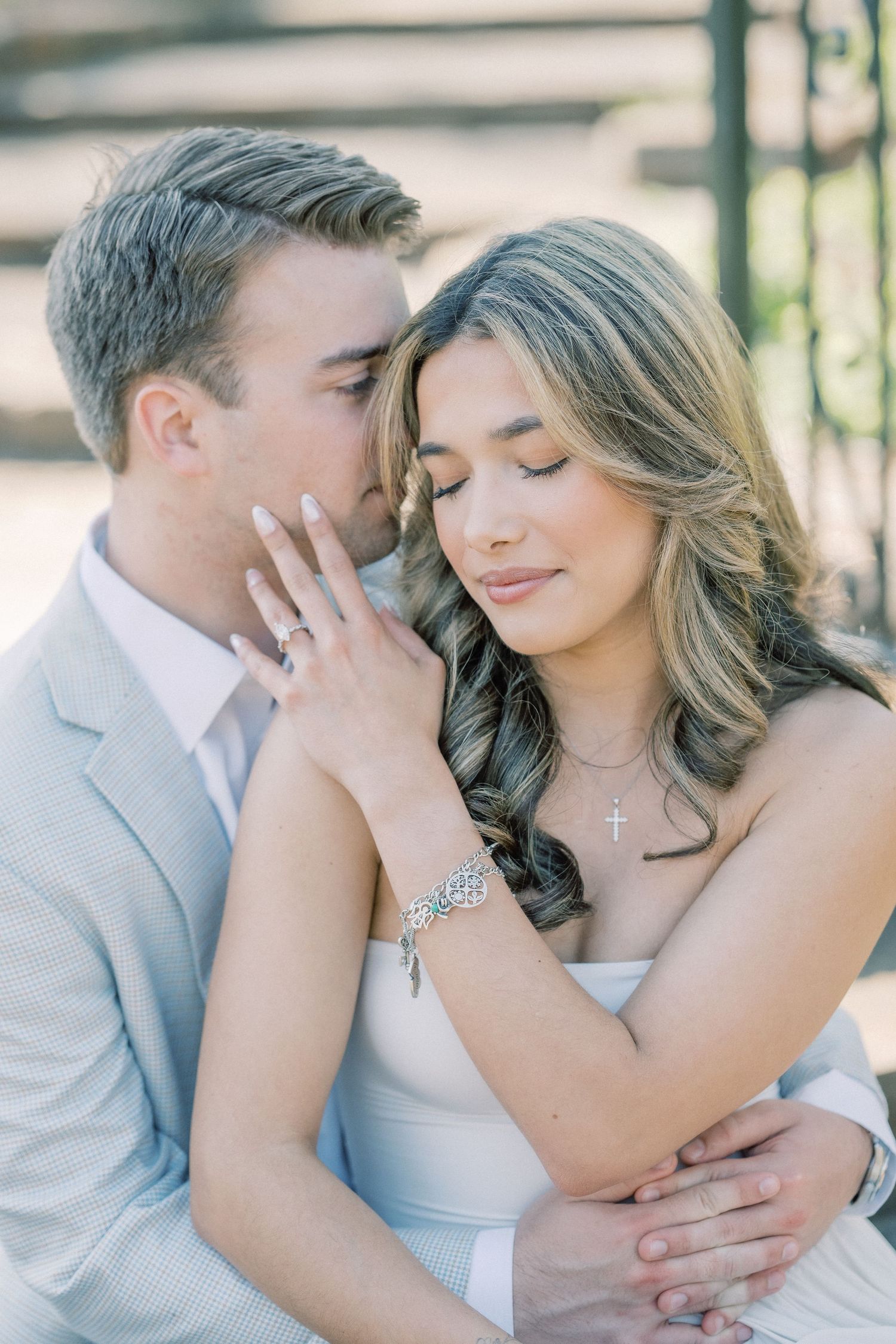 Romantic engagement photo of couple in soft lighting with bride wearing white dress and groom in light gray suit.