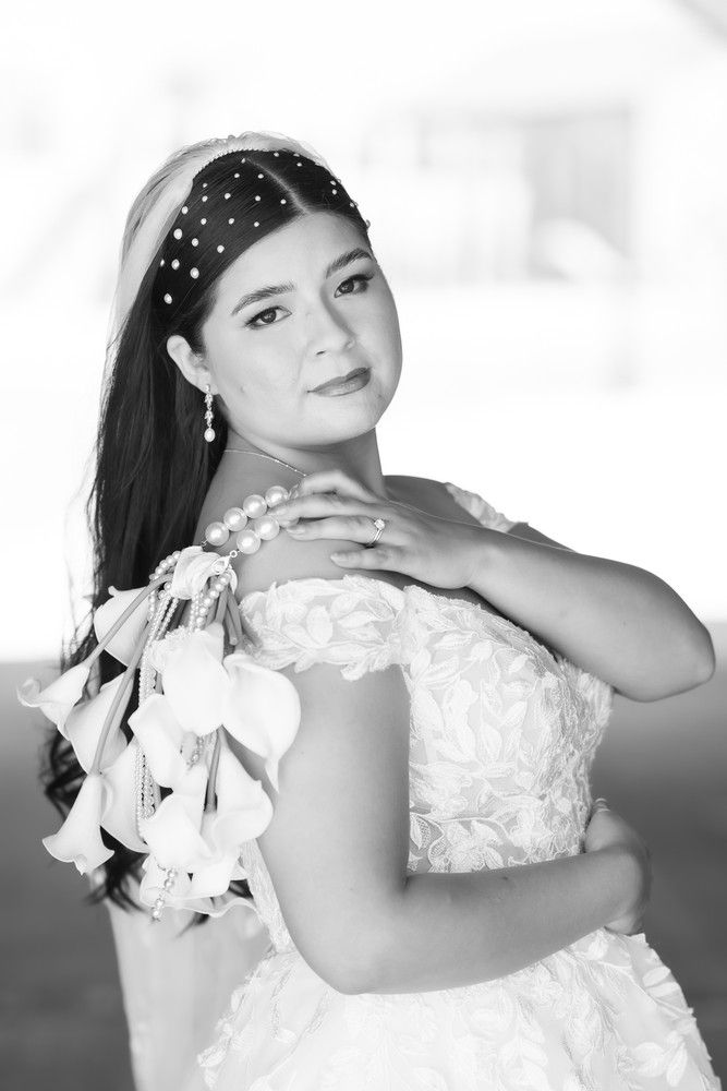 Black and white portrait of a bride wearing a pearl-adorned headpiece and holding white flowers.