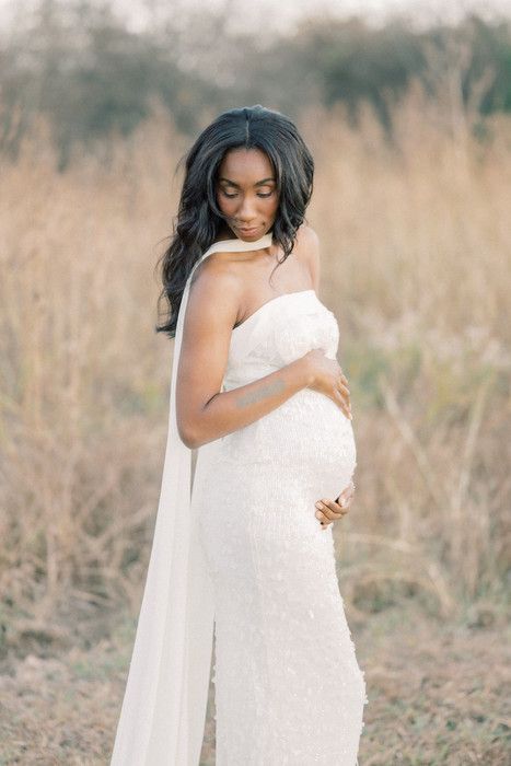 A beautiful maternity photo in a white dress standing in a golden field at sunset.