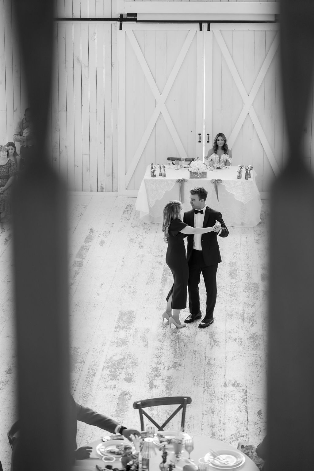 Black and white photo of a couple dancing at an elegant wedding reception in a rustic barn venue.