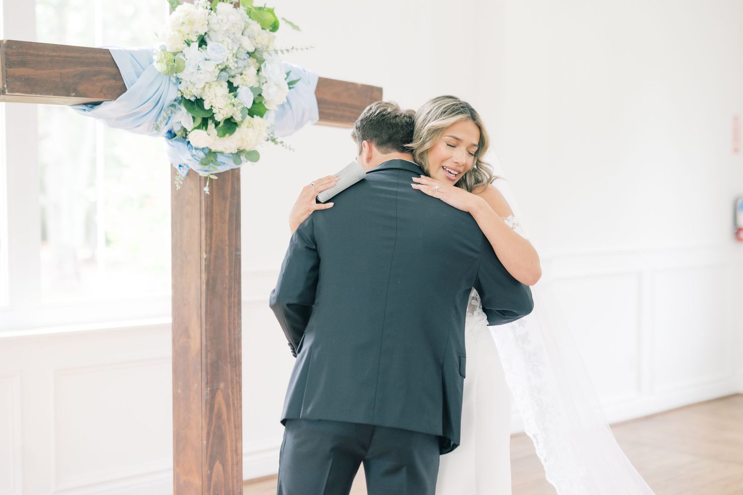 Bride and groom share an emotional embrace near wooden cross at altar.