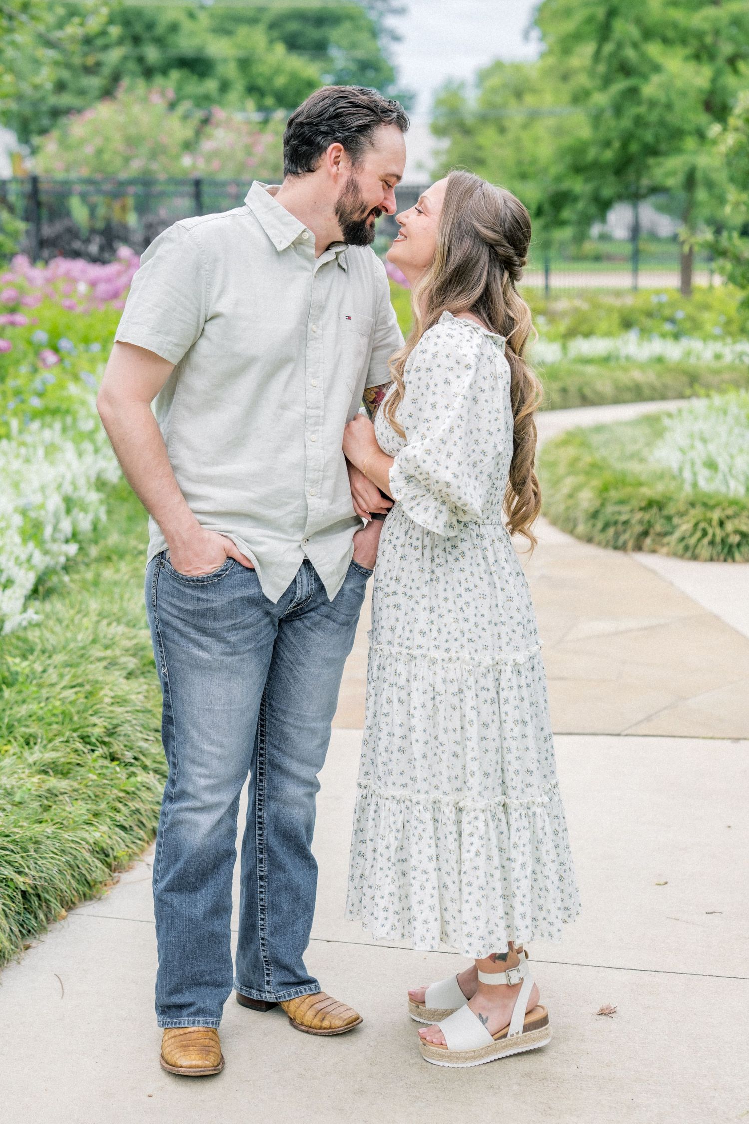 Romantic couple leaning in for a kiss on a scenic garden pathway with blooming flowers.
