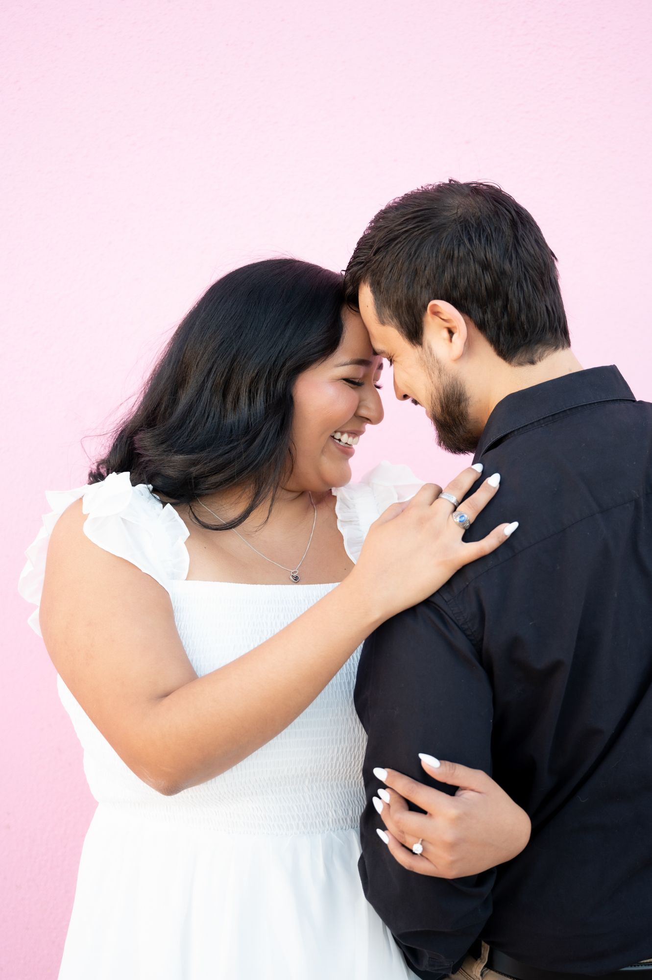 Sweet couple moments captured against pink wall showing genuine emotion and connection.