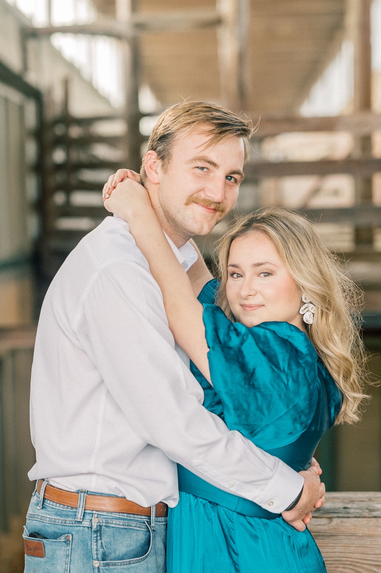 Intimate portrait of couple embracing near wooden railings with soft natural light.