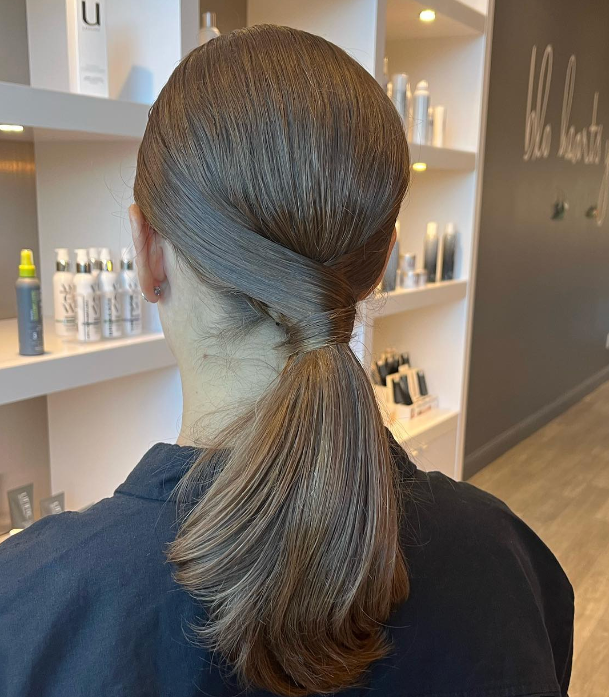Sleek low ponytail hairstyle with smooth, polished finish at a professional hair salon.