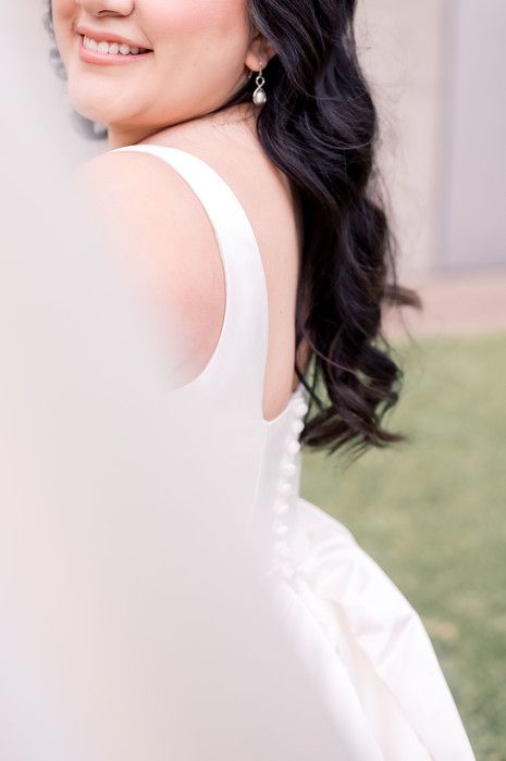 Close-up of a bride in a white sleeveless gown with pearl drop earring and dark curly hair.