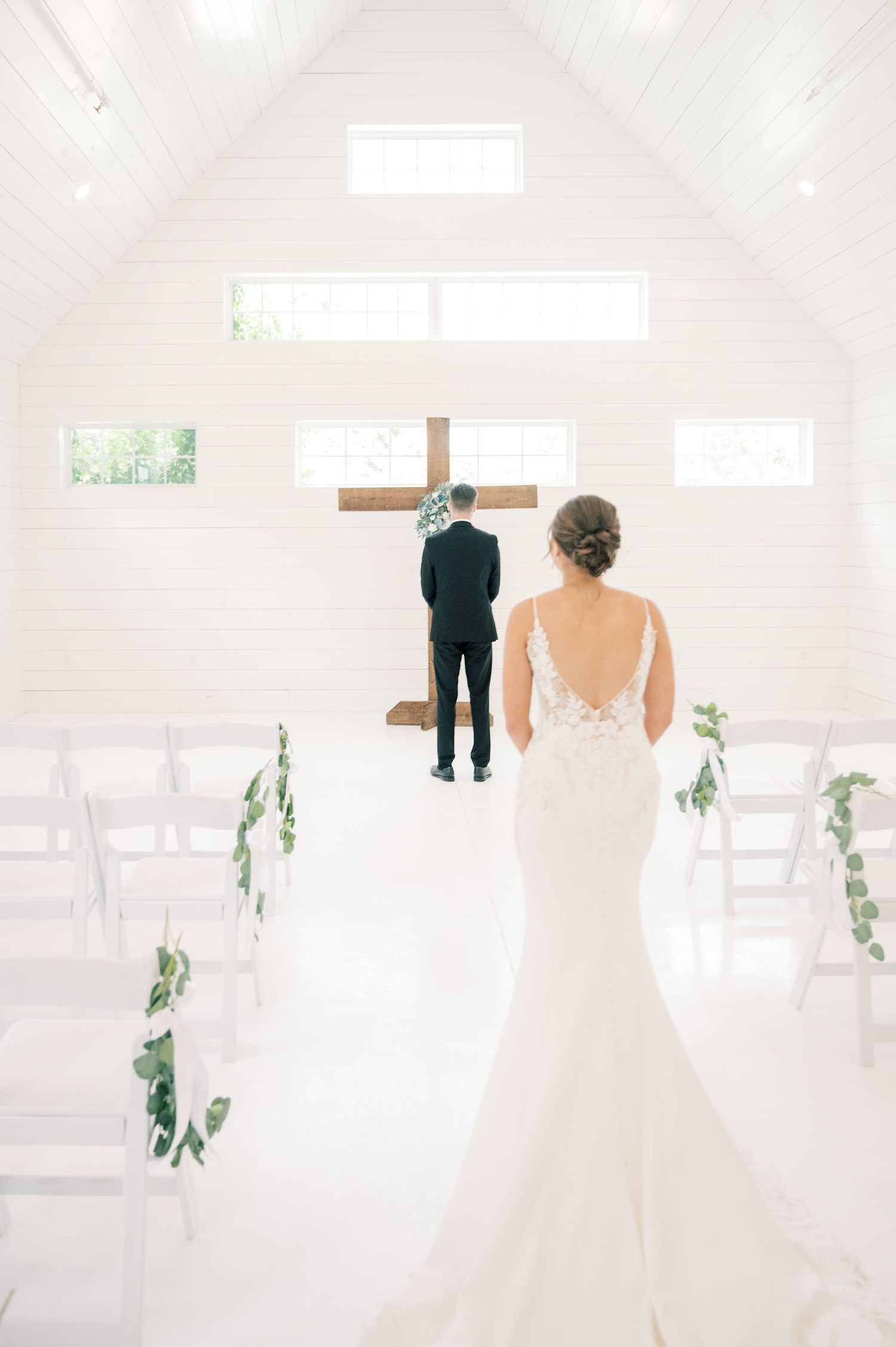A bride and groom share an intimate first look moment in a bright white chapel with wooden accents.