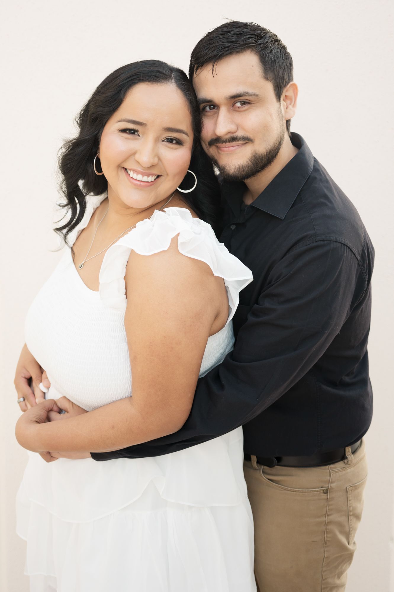 A romantic couple in white and black attire embrace in a series of candid poses against a light background.