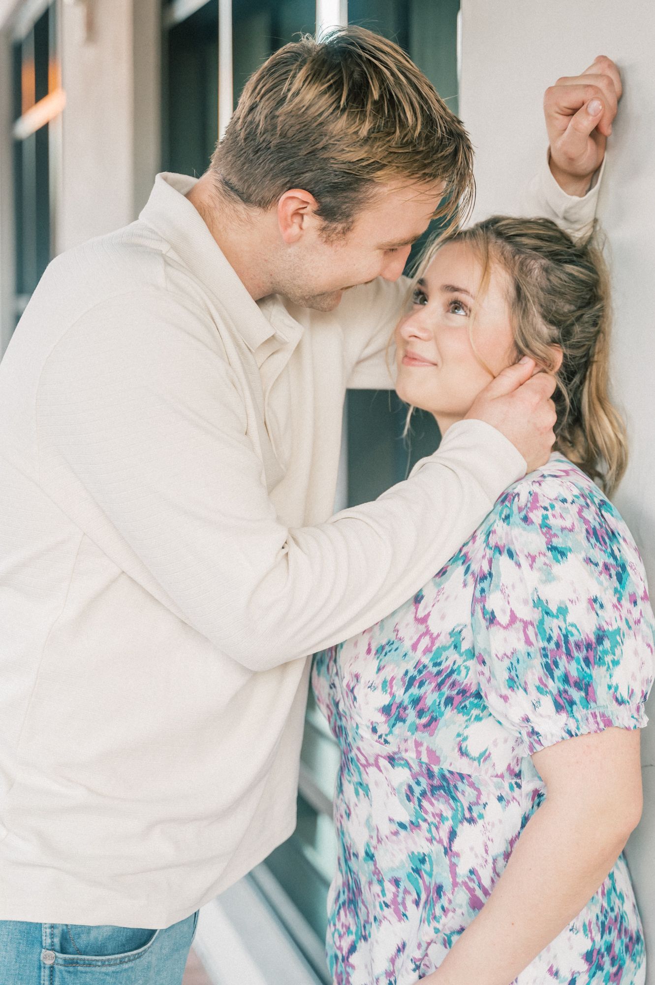 A couple embraces and shares intimate moments against a building wall in matching casual outfits.