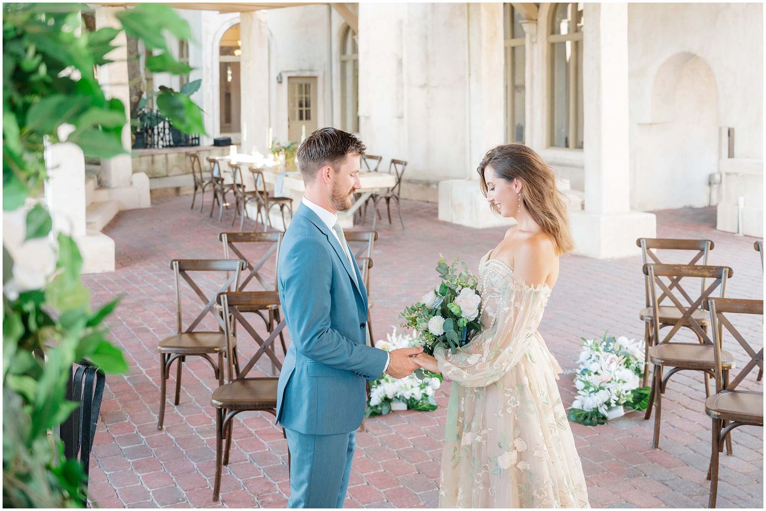 Romantic outdoor wedding ceremony setup with white floral arrangements and wooden cross-back chairs.