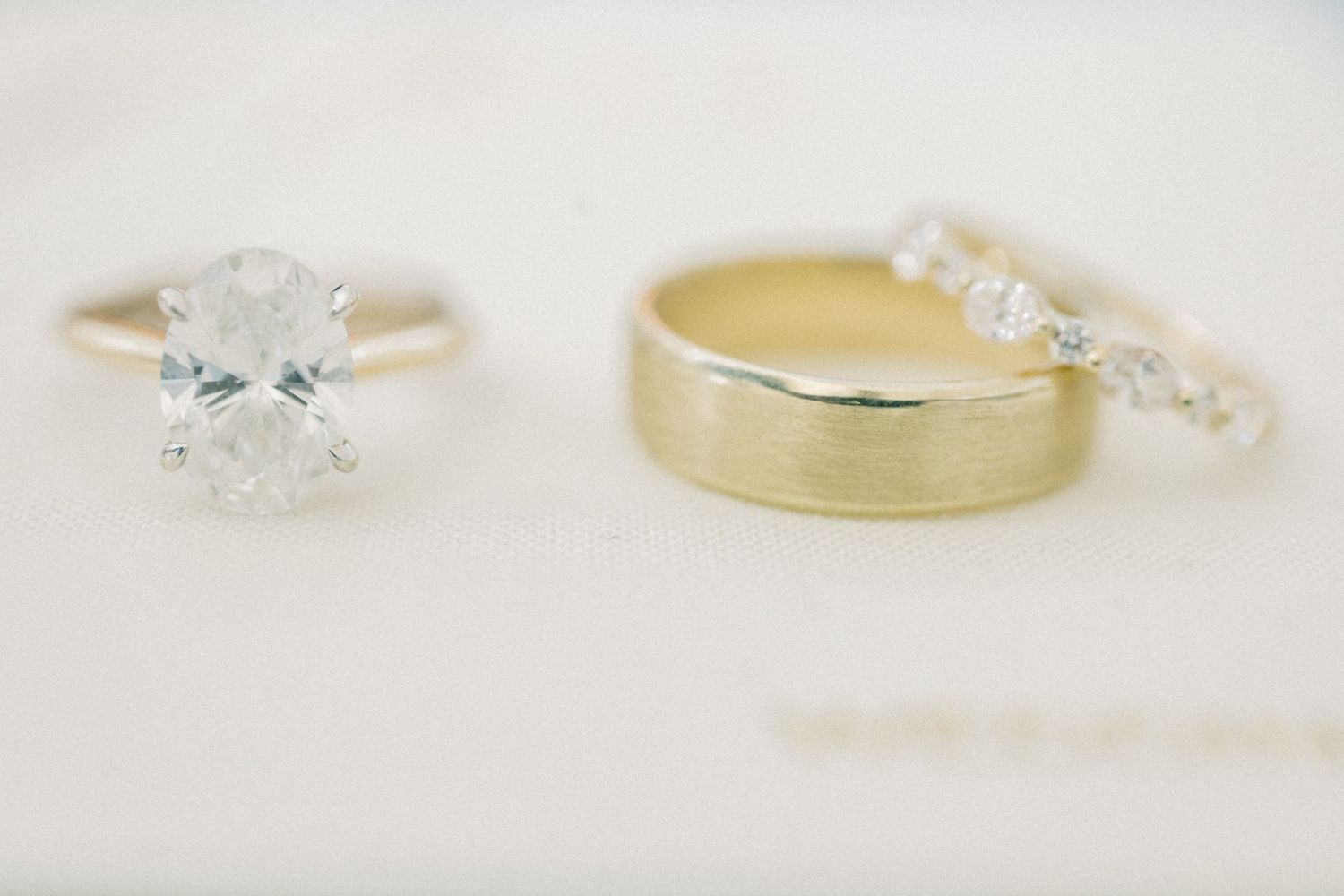 Three wedding rings displayed together, including a solitaire diamond engagement ring, gold band, and diamond eternity band.