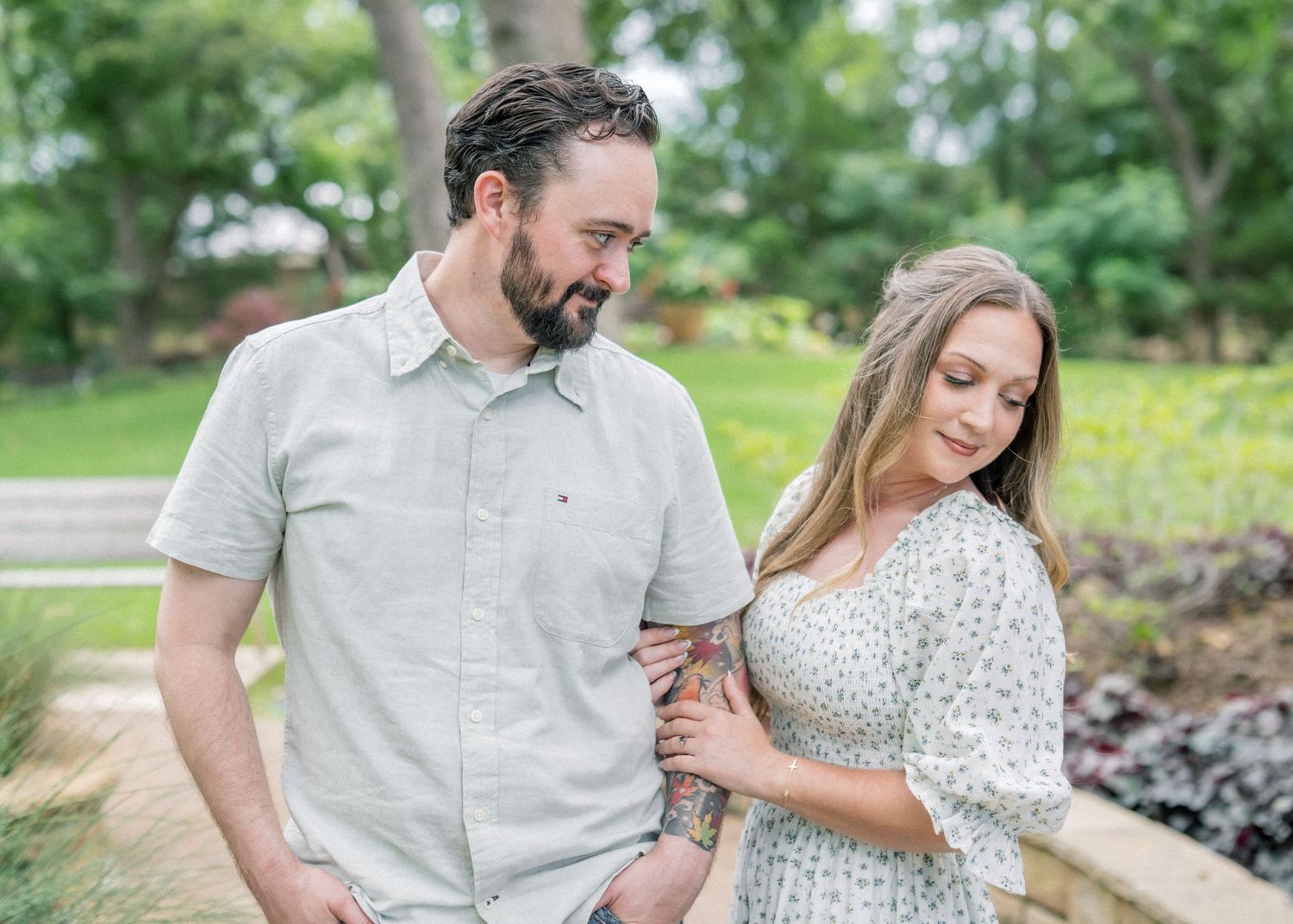 Couple sharing a tender moment in a lush green garden, man in gray shirt and woman in floral dress.