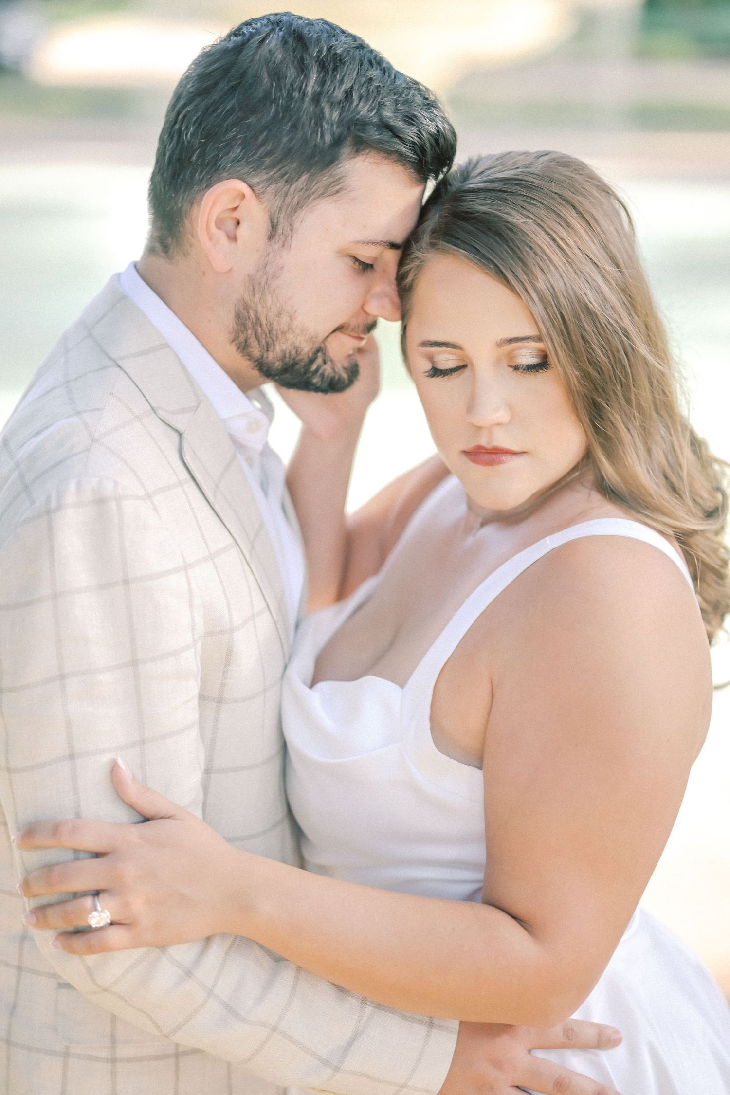 Couple with closed eyes embrace foreheads together in a romantic engagement portrait, her ring visible on his shoulder.